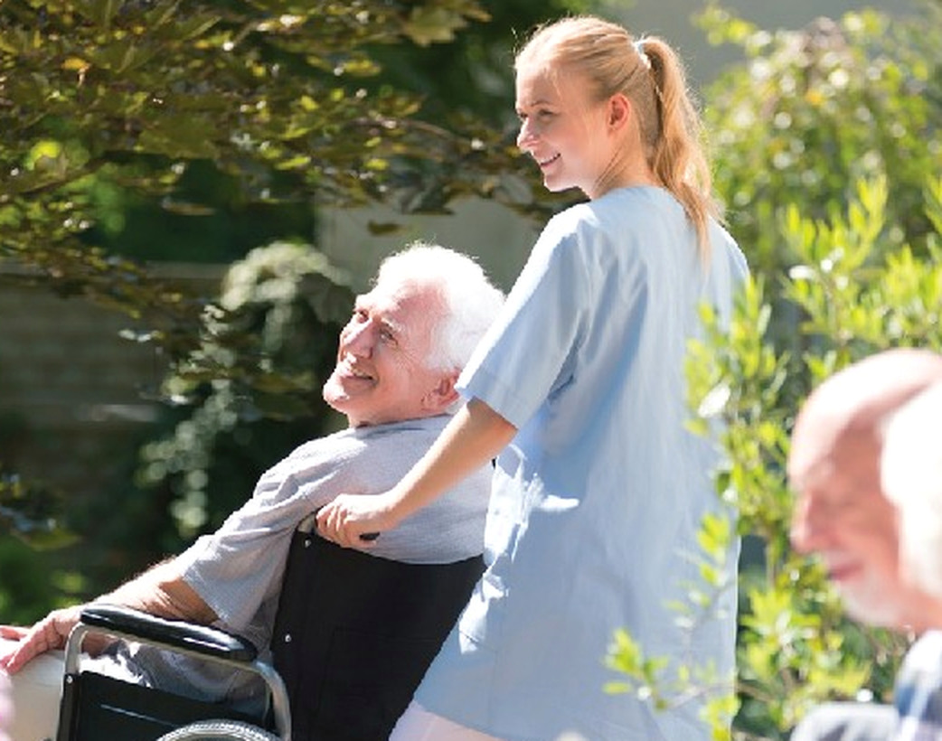 Caregiver with a smiling older adult in a wheelchair outdoors